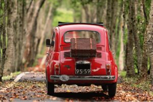 red car driving down road with trees