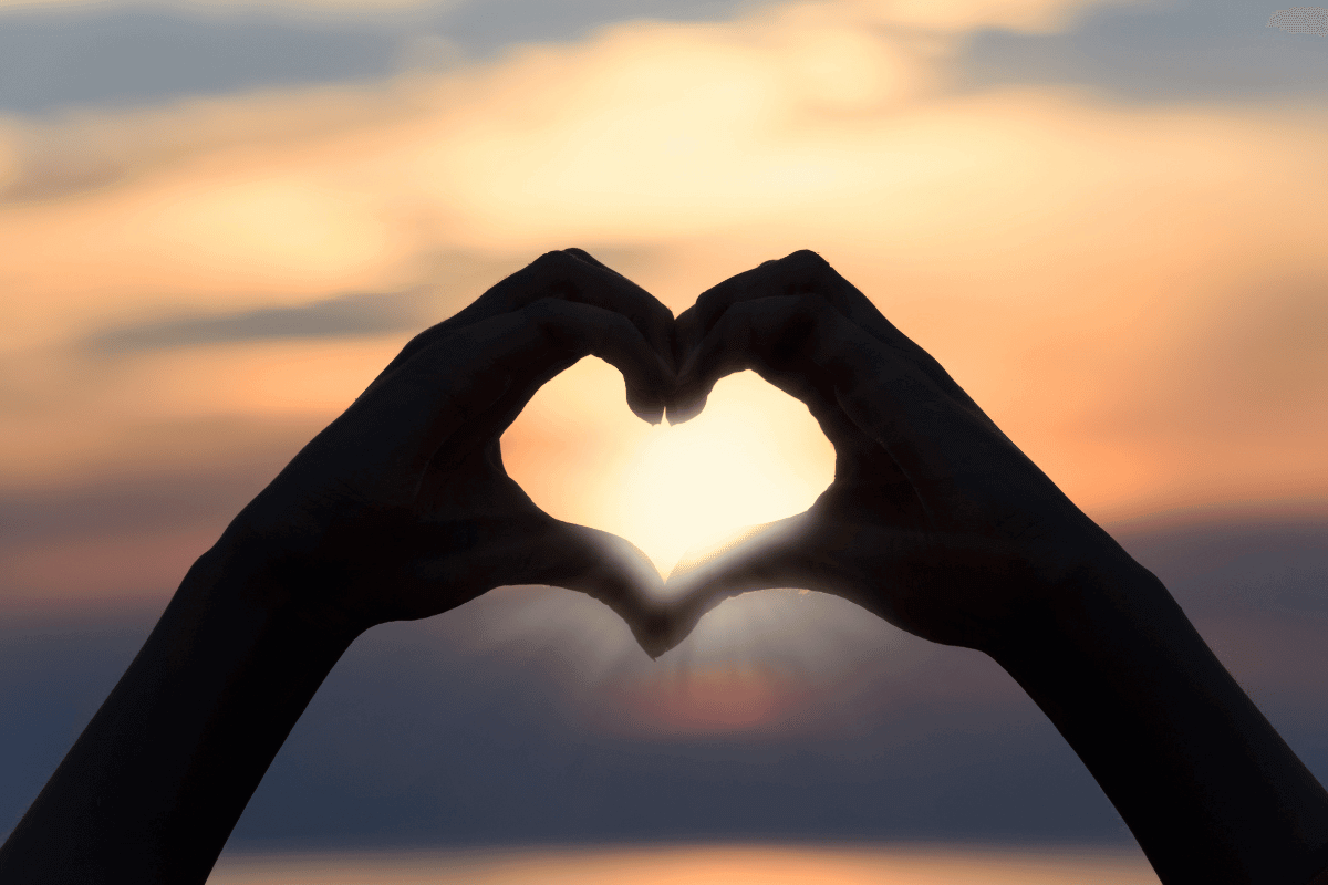 Hands in the shape of a heart with the sun behind